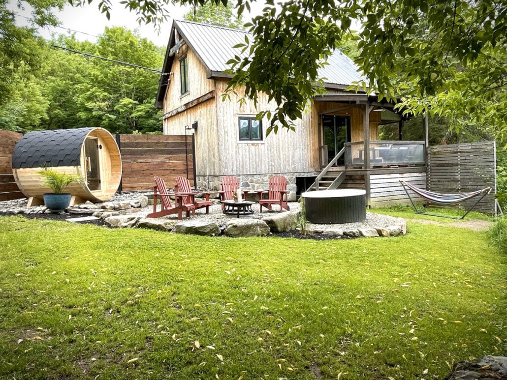 Cour arrière d'un chalet avec sauna tonneau, foyer et chaises Adirondack
